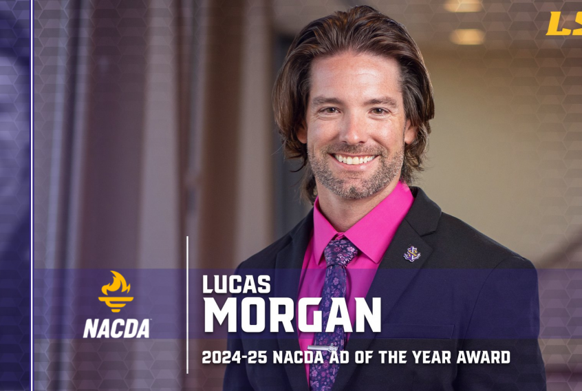 This is a picture of Lucas Morgan. He has brown hair, and brown eyes. He is wearing a black suit with a pink button-up and a purple tie with light and dark purple flowers on it.